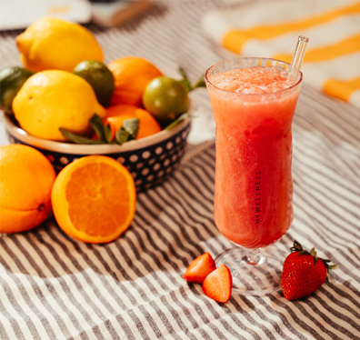 Erfrischender Erdbeer-Smoothie im MyWellness-Glas neben einer Schale mit frischen Zitrusfrüchten