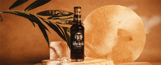 ritz-Kola Original Flasche auf einem Natursteinpodest vor warmen Erdtönen