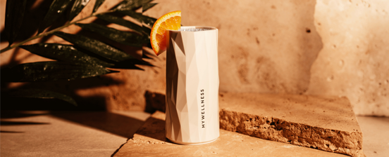 Weißes facettiertes MyWellness-Glas mit Orangenscheibe auf einem Natursteinuntergrund