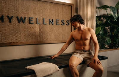 Mann sitzt auf der Hydrojet-Massageliege vor dem MyWellness-Logo in der Suite