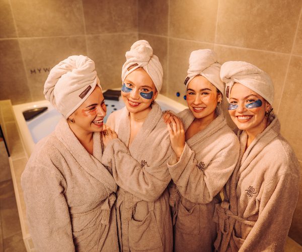 Vier Frauen mit Handtuch-Turbanen und Augenpads in MyWellness-Bademänteln vor dem Whirlpool